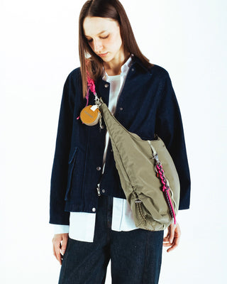 Person wearing a navy jacket with a green sling bag with keychains hanging on a white background