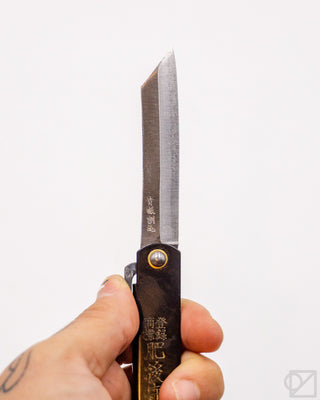 Pocket knife close-up: satin blade with black handle and circular gold pin