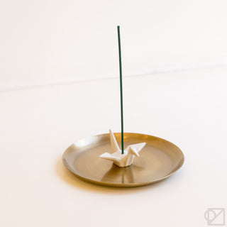 White origami crane incense burner on round dish with green incense stick