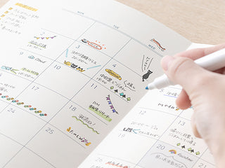 Hand holding a paintable stamp over a monthly calendar page with printed date squares