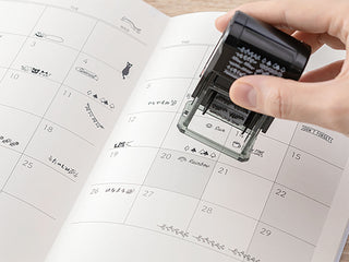 Monthly paintable rotary stamp pressing onto a calendar grid page with small icons