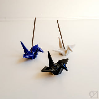 Assorted origami crane incense burners: blue, white, and black with sticks
