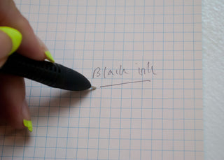 Hand holding a black multi-pen writing on blue grid paper