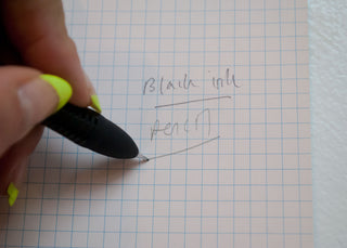Black multi-pen tip writing on blue grid paper held by a hand