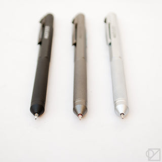Three multi-pens with metal tips and textured barrels in black, gunmetal gray, and white