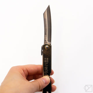 Pocket knife held in hand, narrow chrome blade with dark handle and brass rivet